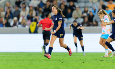 Sally Menti wearing a dark blue uniform jumps in the air and celebrates on a soccer field