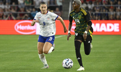 Two players chase after a ball on a soccer field